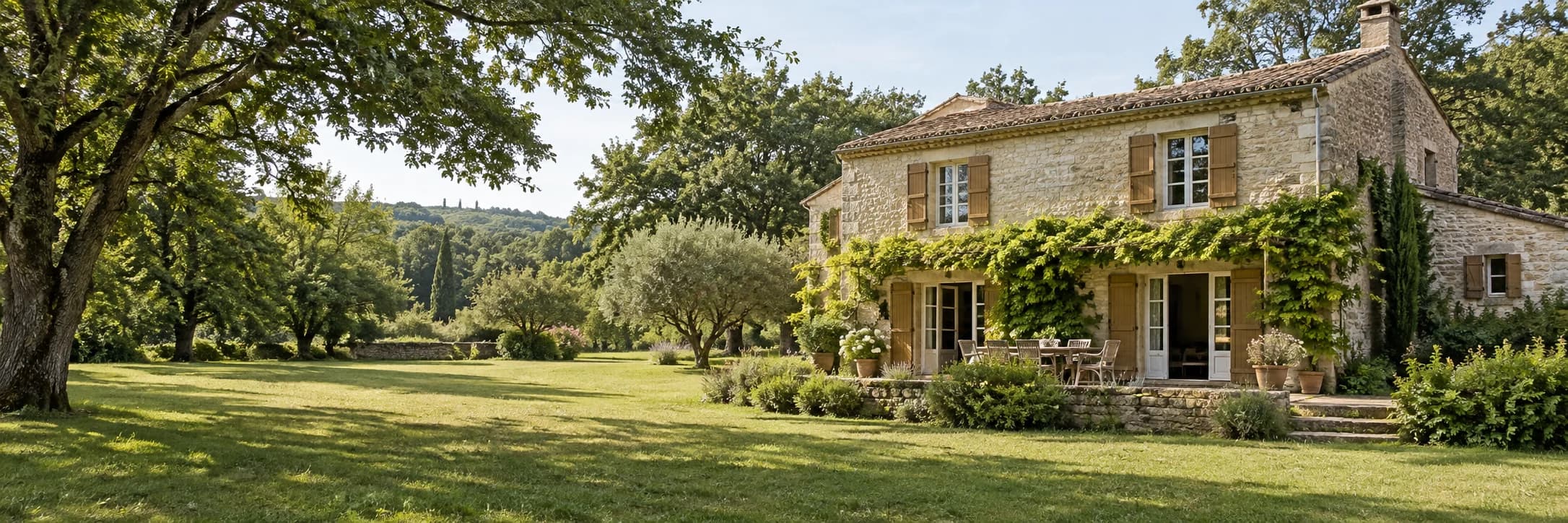 Une maison de campagne en pierre ouverte sur une terrasse et un jardin arboré